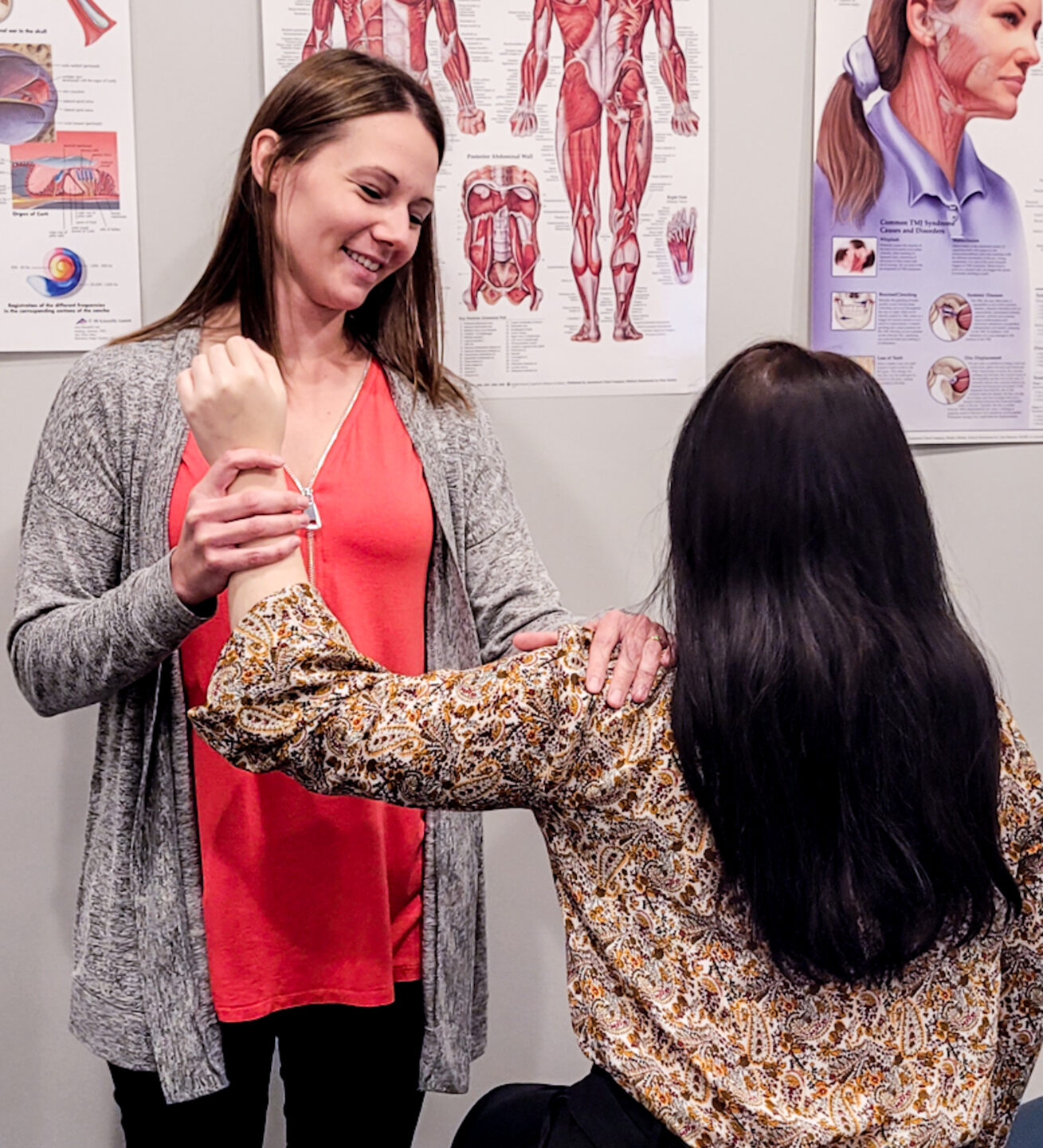 Nycole a physiotherapist, holding a patient's arm up at a right angle, stretching shoulder